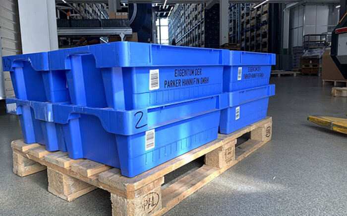 Blaue Mehrweg-Transportkisten der Parker Hannifin GmbH auf einer Holzpalette in einem Lagerhaus.