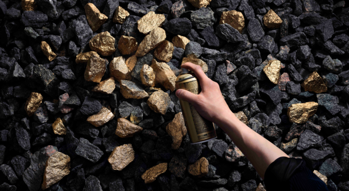 Eine Hand hält eine Sprühdose und sprüht goldene Farbe auf dunkle Steine.