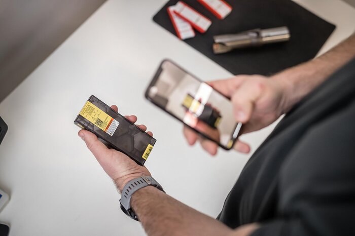 Eine Person fotografiert eine originalverpackte Sandvik-Komponente mit einem Smartphone.