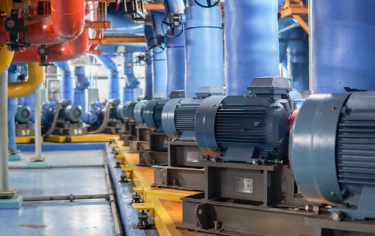 Reihen von Elektromotoren und farbigen Rohren in einer Pumpstation