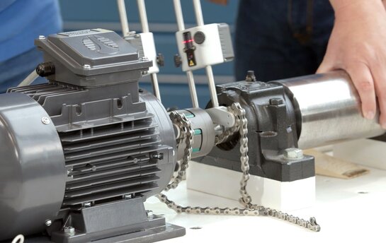 Eine Person arbeitet an der Montage und Wartung einer Industrieanlage mit einem Motor und Kettenantrieb.