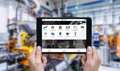 Eine Person hält ein Tablet, das eine Webseite mit verschiedenen technischen Produkten in einer industriellen Umgebung anzeigt.