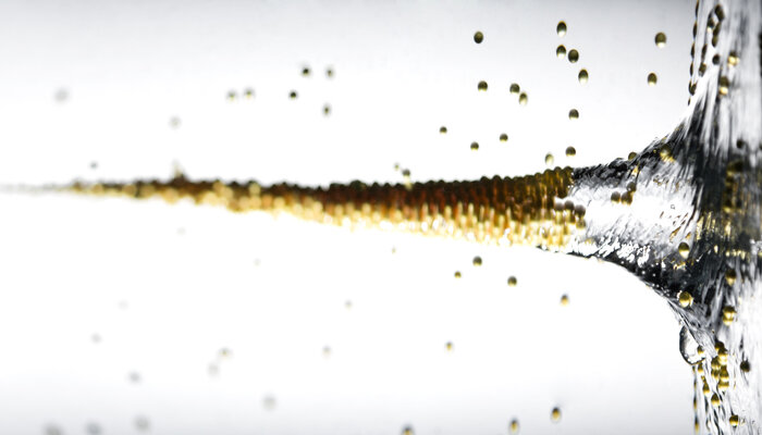 Eine Nahaufnahme von sprudelnder Flüssigkeit, die aus einem Glas gegossen wird, mit vielen kleinen Luftblasen.