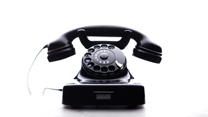 Ein schwarzes, klassisches Wählscheibentelefon vor hellem Hintergrund.