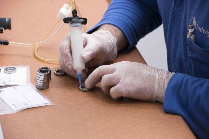 Eine Person in blauen Handschuhen verwendet eine Spritze, um Spezialfett auf kleine Lager aufzutragen.