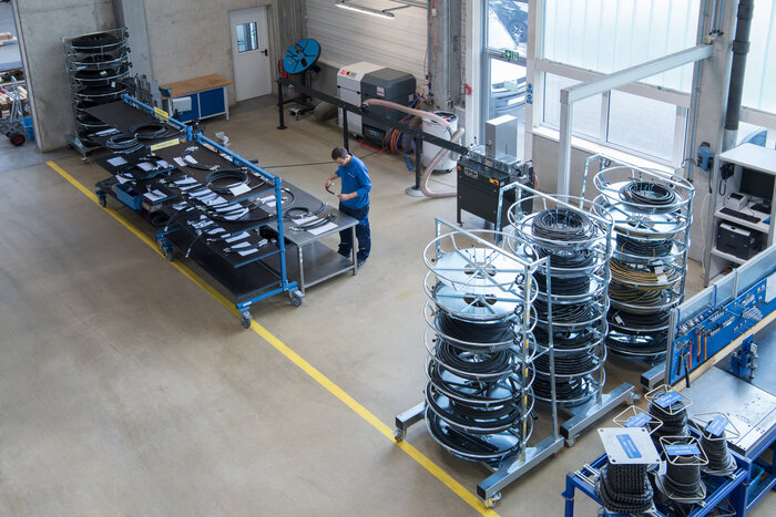 Ein Mann arbeitet in einer Schlauchwerkstatt mit zahlreichen aufgerollten Schläuchen und Arbeitsmaterialien.