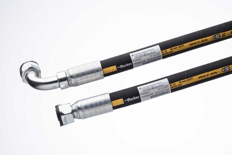 Zwei industrielle Schläuche mit Metallanschlüssen und Etiketten auf hellem Hintergrund.