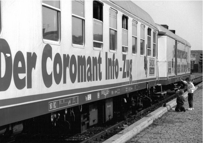 Ein Zug mit der Aufschrift "Der Coromant Info-Zug" steht auf einem Gleis; zwei Kinder betrachten ihn neugierig.