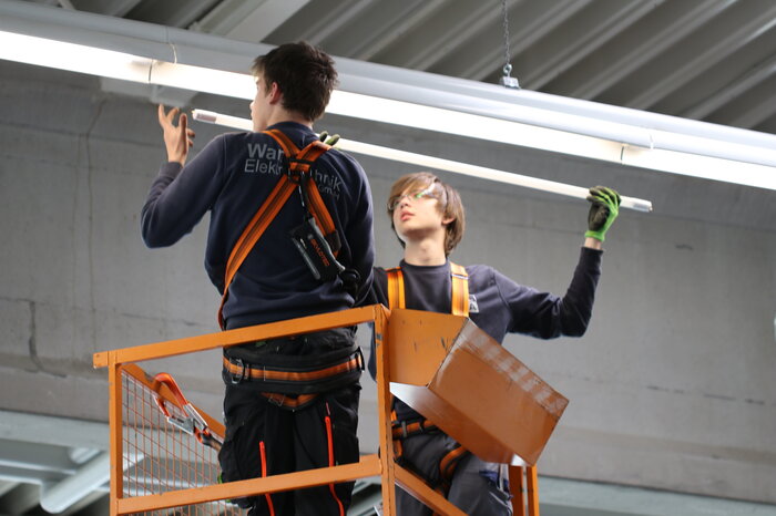 Zwei Personen installieren eine LED-Leuchte in einer Industriehalle.