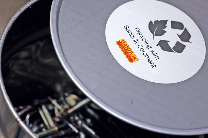 Eine Metalltonne mit einem Aufkleber, der Sandvik Coromants Recycling-Programm für Hartmetall bewirbt.