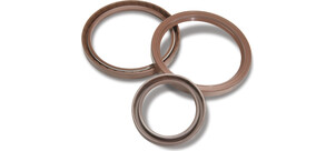 Drei unterschiedlich große, braune Wellendichtungen aus Kunststoff liegen kreisförmig angeordnet auf einer weißen Oberfläche.